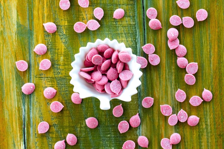 Ruby chocolate chips spread out on a green wood surface