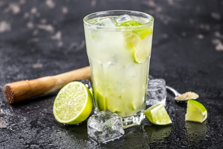 A lime cocktail next to limes, a muddler and brown sugar