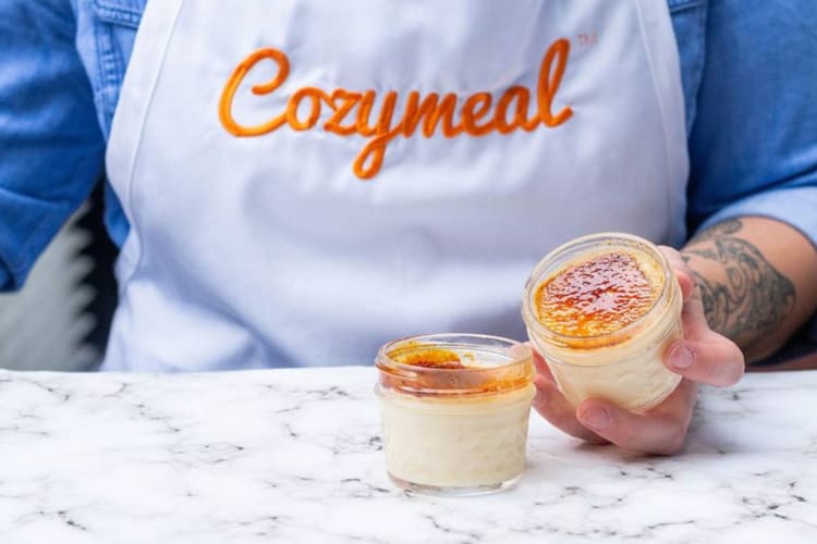 A person in a Cozymeal apron with potted creme brulee