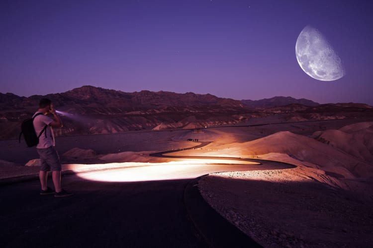 A person hiking on a winding road under the moon at night