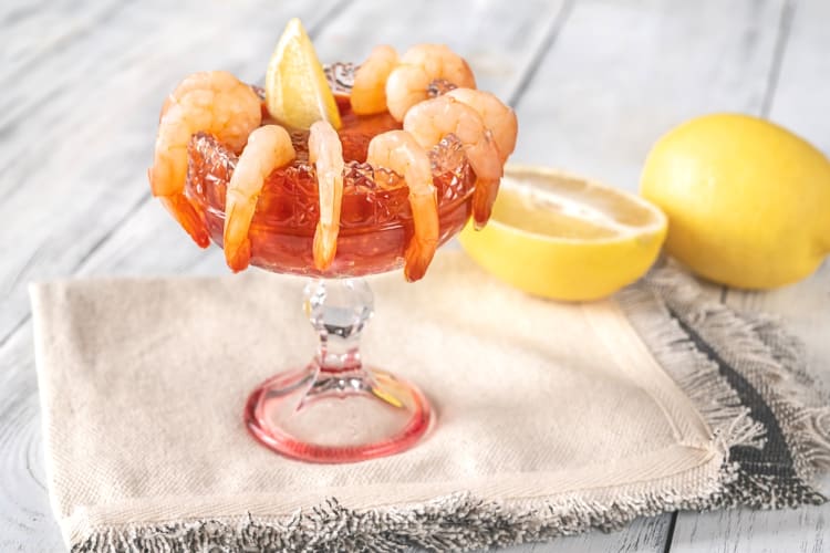Shrimp cocktail on a napkin next to a lemon and lemon wedge