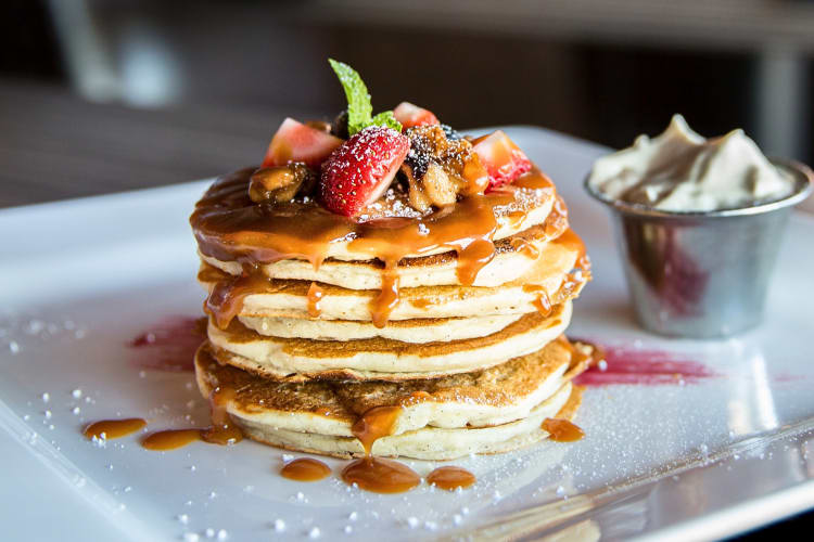 Stack of seven pancakes topped with pieces of fruit and syrup