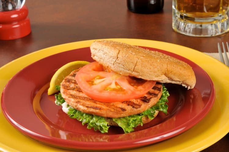 Salmon burger with lettuce and tomato on a plate next to a lemon wedge