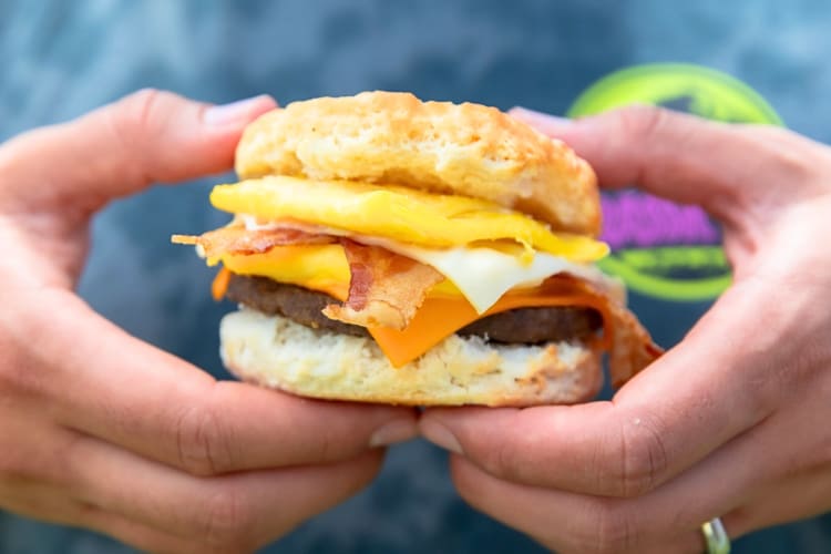 Person's hands holding a sausage, egg, bacon and cheese biscuit from Carl's Jr.