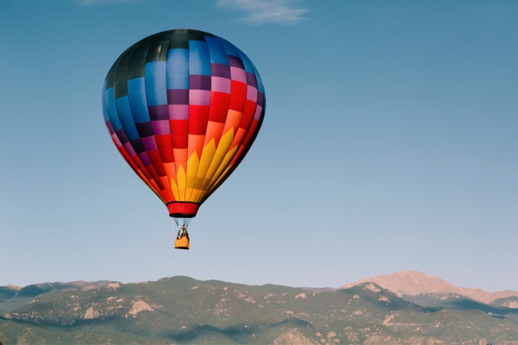 A colorful hot air balloon over a greenery-covered hill