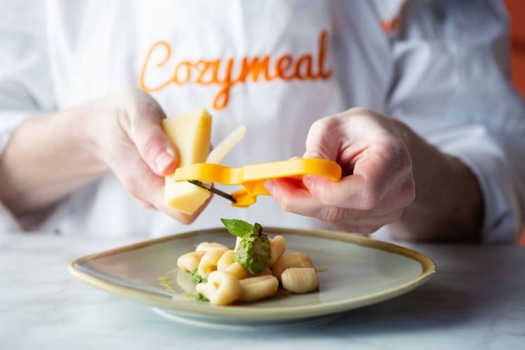 A person grating cheese onto a plate of gnocchi