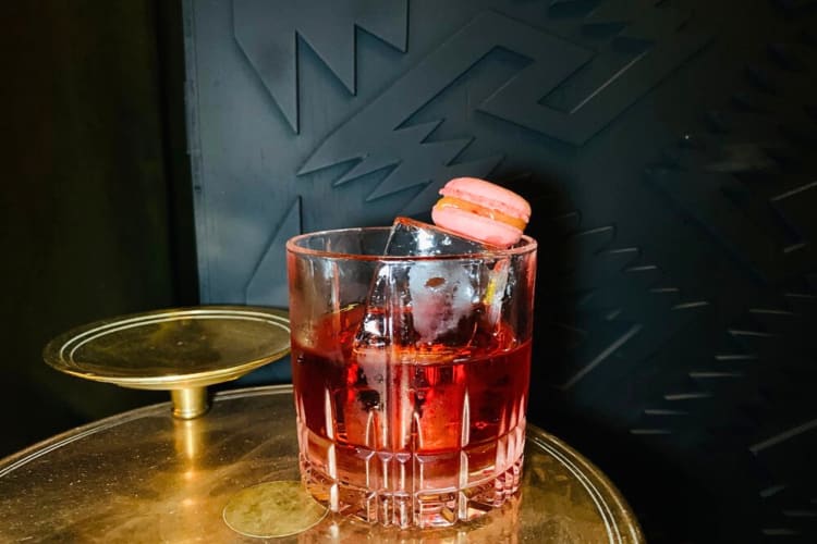 Dark orange cocktail in a tumbler with a macaroon on the top from Selva Oaxaca Cocktail Bar