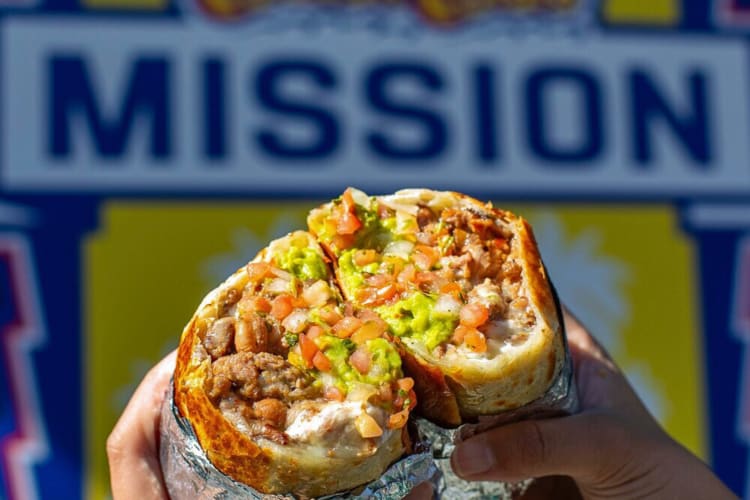 Hands holding two halves of a burrito from Señor Sisig, a Filipino restaurant in San Francisco