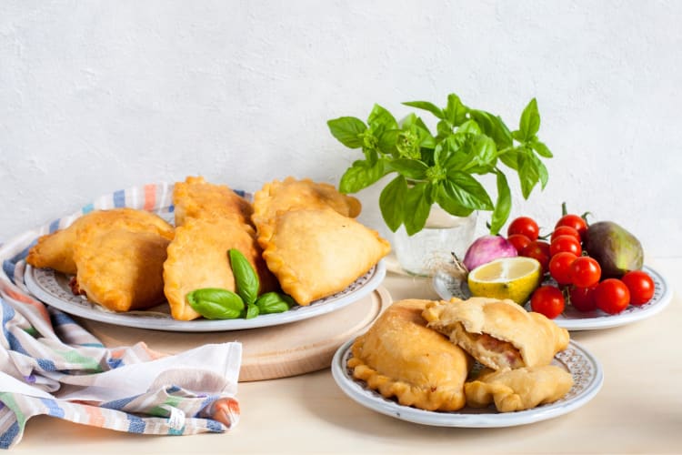 Fried pastry turnovers next to a basil plant and plate of vegetables