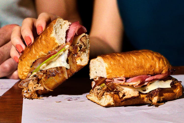 Person's hand picking up half of a meaty and cheesy sandwich from Potbelly