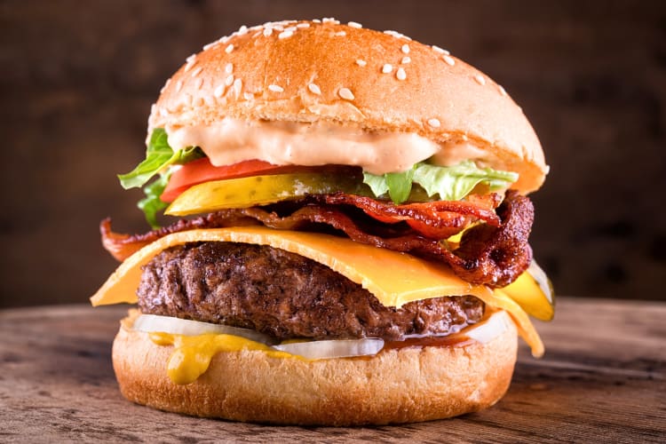Side view of a burger with cheese, onions, pickles, lettuce, tomato and bacon