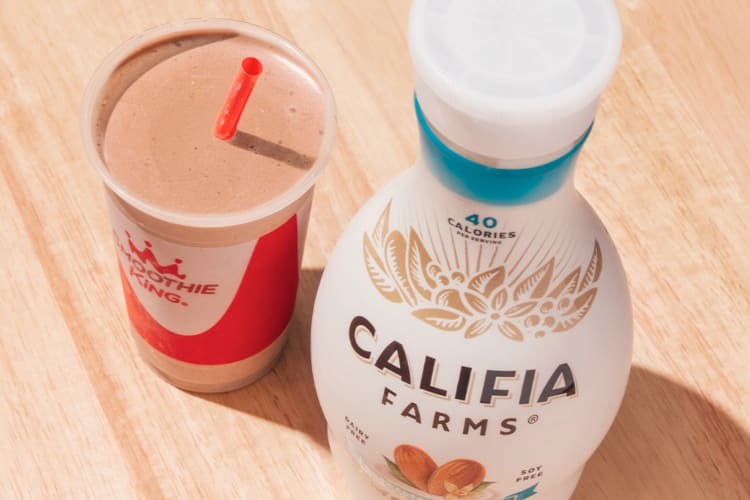 A chocolate smoothie next to a container of almond milk