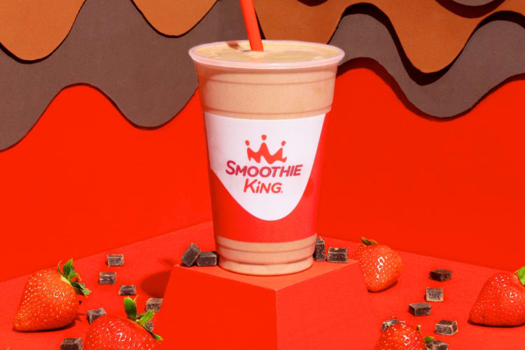 A chocolate-strawberry smoothie next to fresh strawberries and chocolate chunks