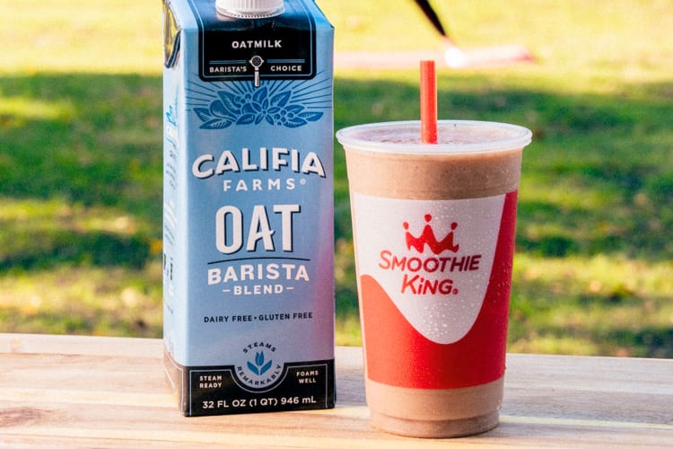 An apple smoothie next to a carton of oat milk