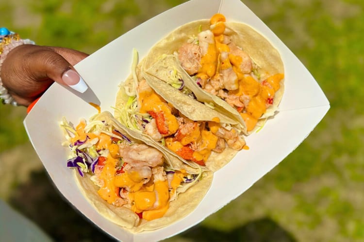 Close-up of a woman's hand holding a paper tupperware with tacos in it