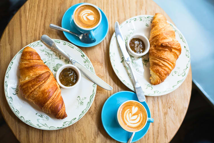 Aerial shot of two croissants with side sauces and two cappuccinos 