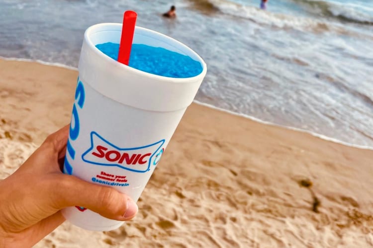 A person holding a blue drink at the beach