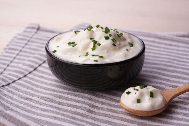Spoonful of sour cream next to a bowl of sour cream
