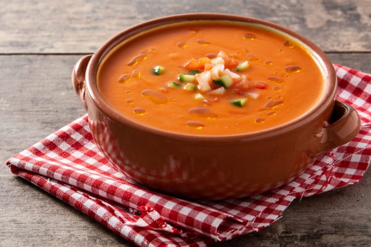 A bowl of gazpacho sitting on a red and white cloth