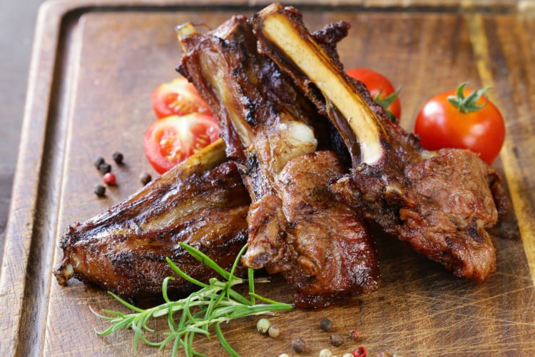 Lamp chops on a wooden serving board with green garnish and tomatoes