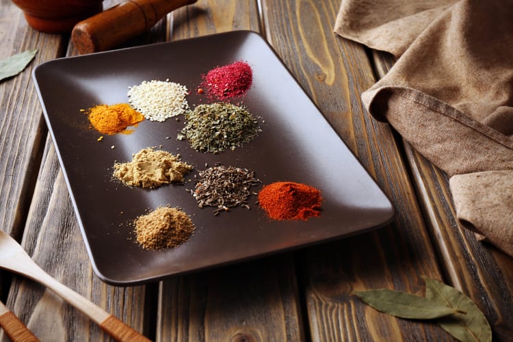 Eight heaps of different spices on a black serving tray