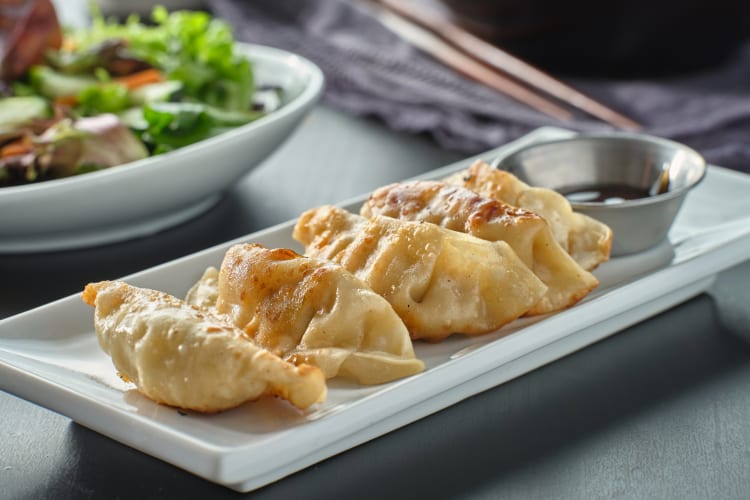 Four dumplings with sauce on the side, and salad in the background
