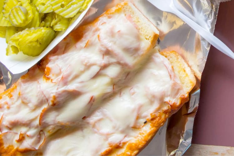 An open-faced sandwich with melted cheese on a tray with pickles
