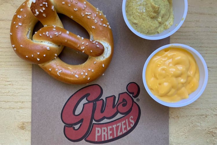 A pretzel next to two sauces and a Gus' Pretzels bag