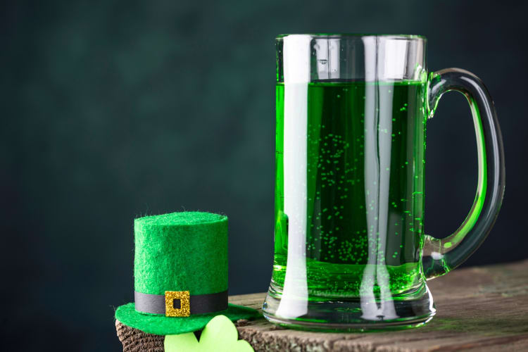 A pint of green beer next to a small hat decoration