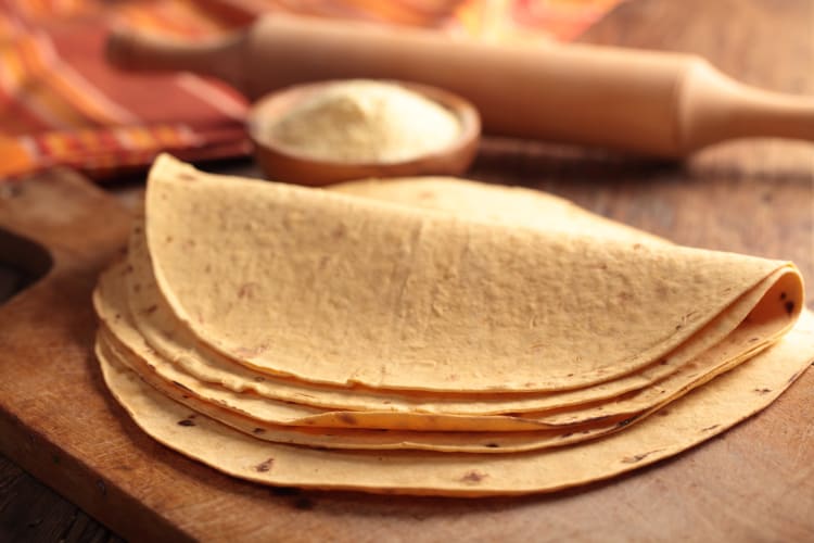 Stack of tortillas with a bowl of flour and a rolling pin in the background