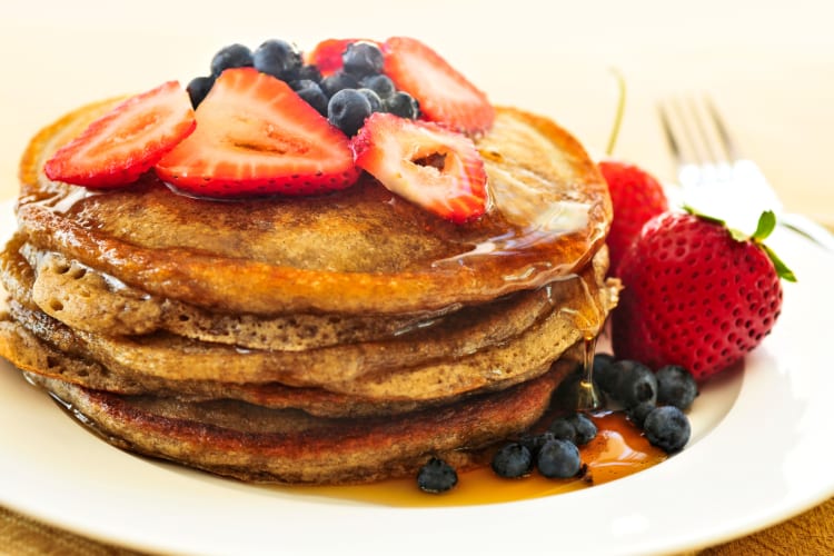 Stack of pancakes with blueberries, strawberries and honey on top