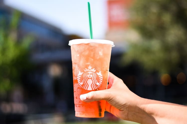 An orange-pink iced drink in a Starbucks cup