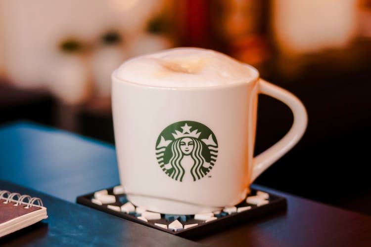 A Starbucks mug on a coaster with a hot drink in it