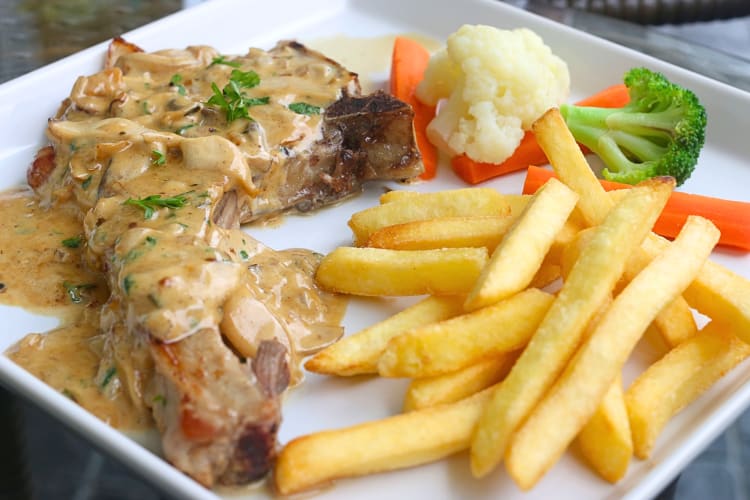 Pork chop smothered in sauce with a side of vegetables and fries