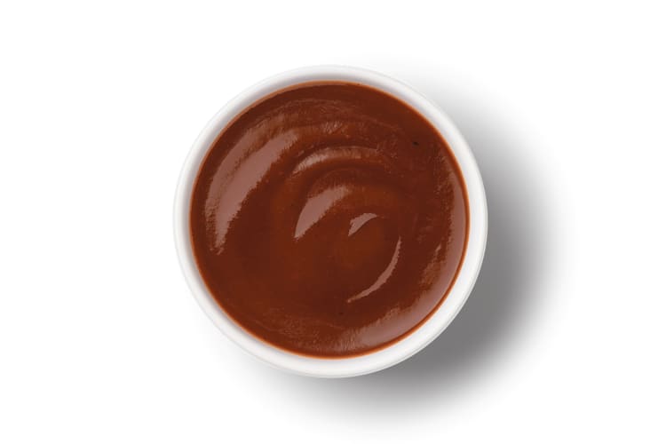 A small, white dish with barbeque sauce in it