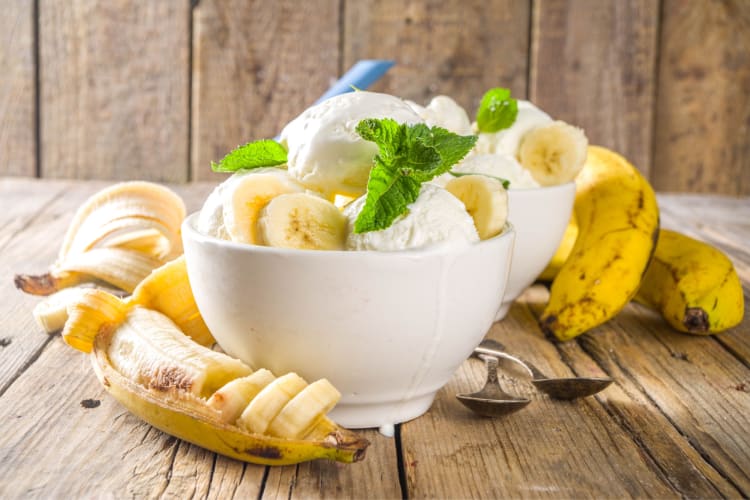A bowl of banana ice cream next to fresh bananas