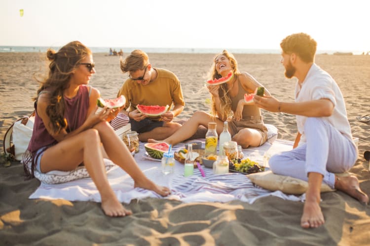 Four people on a blanket at the beach eating watermelon