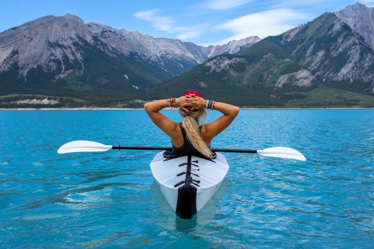A person in a kayak on the water near mountains