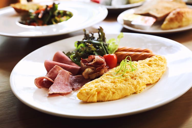 Breakfast with an omelette next to sausage, ham, bacon and a salad