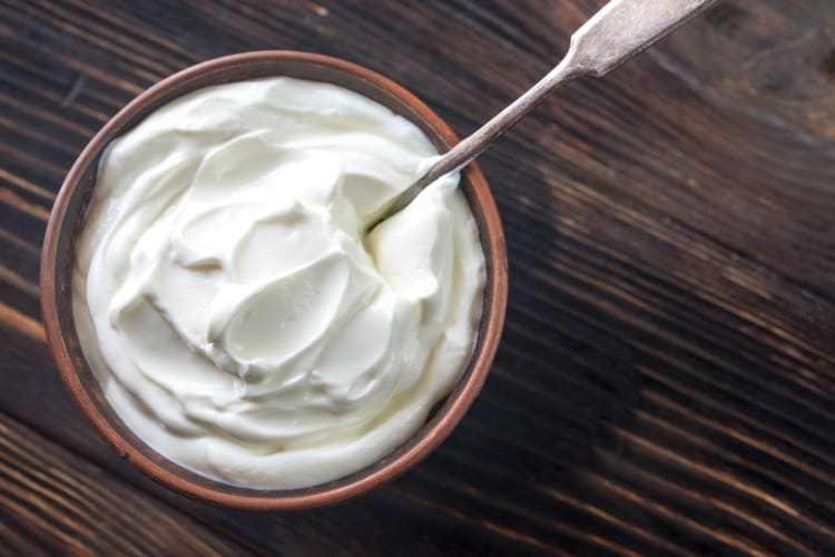 A wooden bowl with Greek yogurt and a metal spoon