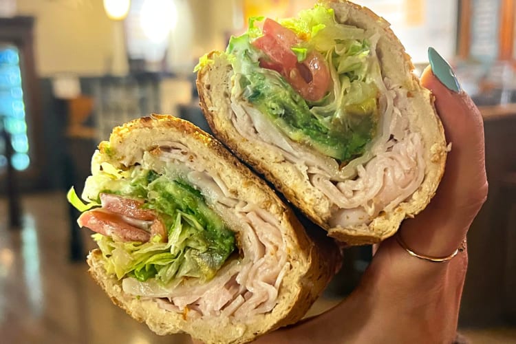 Person's hand holding a sandwich with meat, lettuce and tomato on from Potbelly