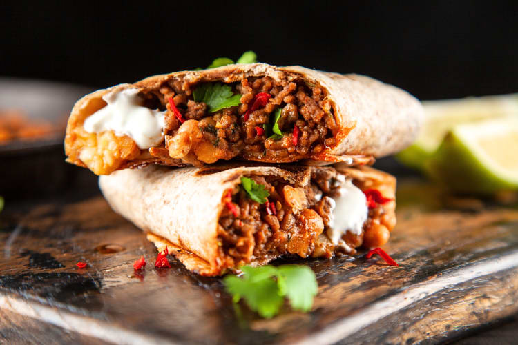 Beef wrap cut in half, sitting on a wooden chopping board