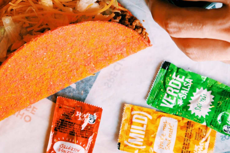 A taco next to red, orange and green hot sauce packets