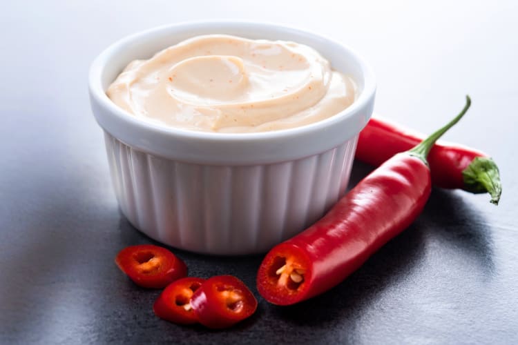 A ramekin with spicy ranch sauce next to chile peppers