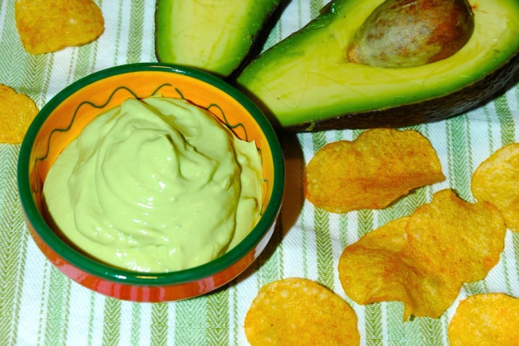 A bowl of blended avocado next to fresh avocado