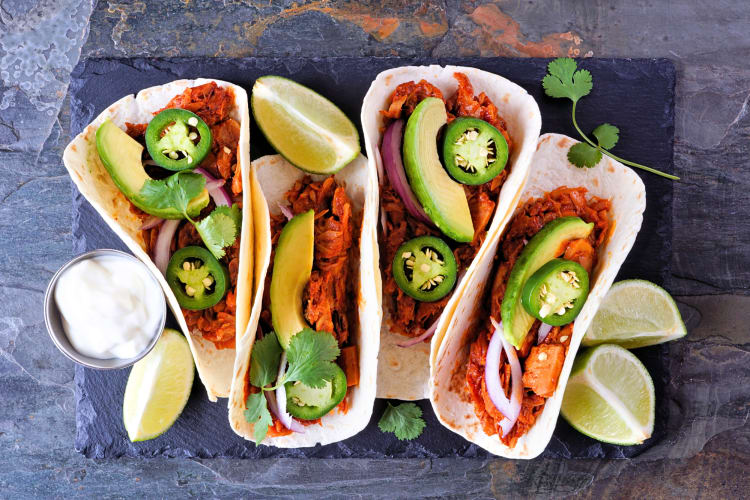 Aerial shot of four jackfruit tacos with avocado, jalapeños and lime wedges