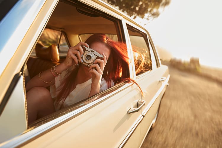 A woman taking photos with a camera while sitting in a car