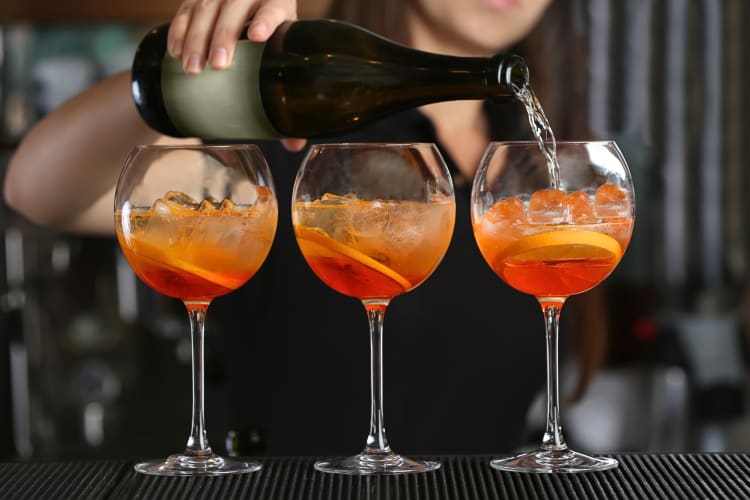 Side view of three cocktails, with a person's hand pouring liquid into one of them