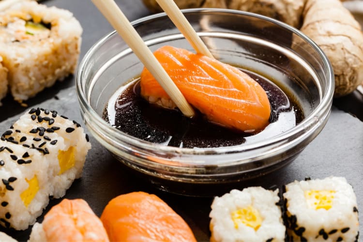 A person dipping salmon sushi in tamari 