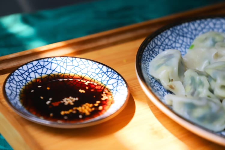 A bowl of tamari next to a plate of dumplings